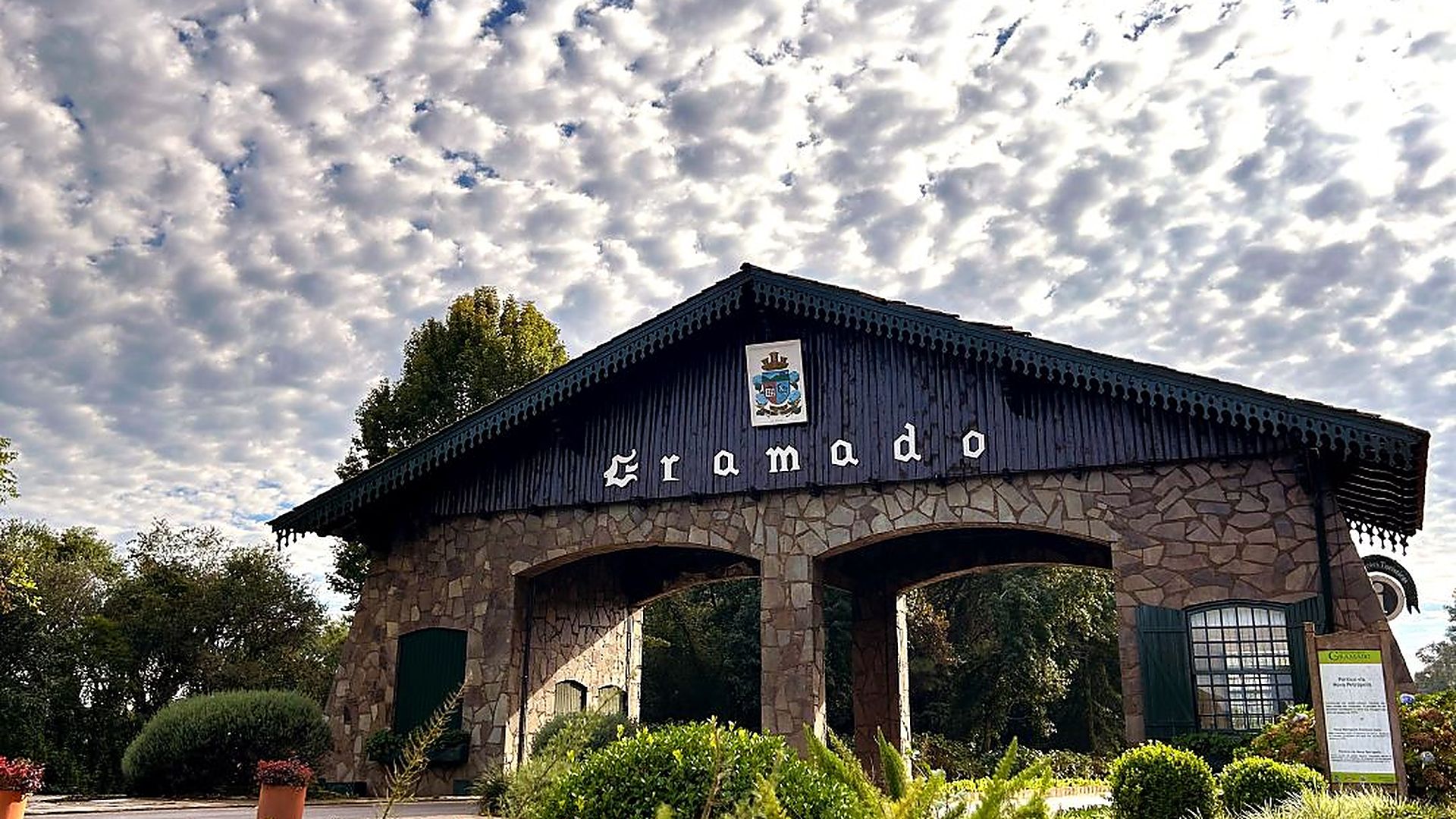 Pórtico de entrada da cidade de Gramado, em pedra e madeira, cercado de flores